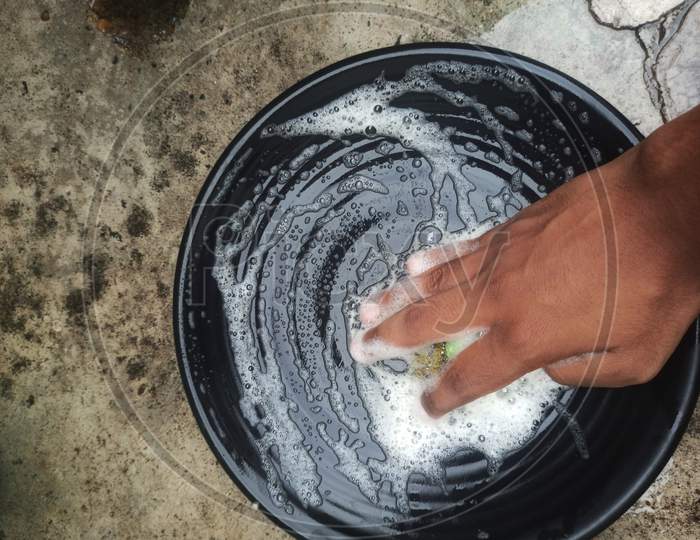 A boy hand washing plate on floor.