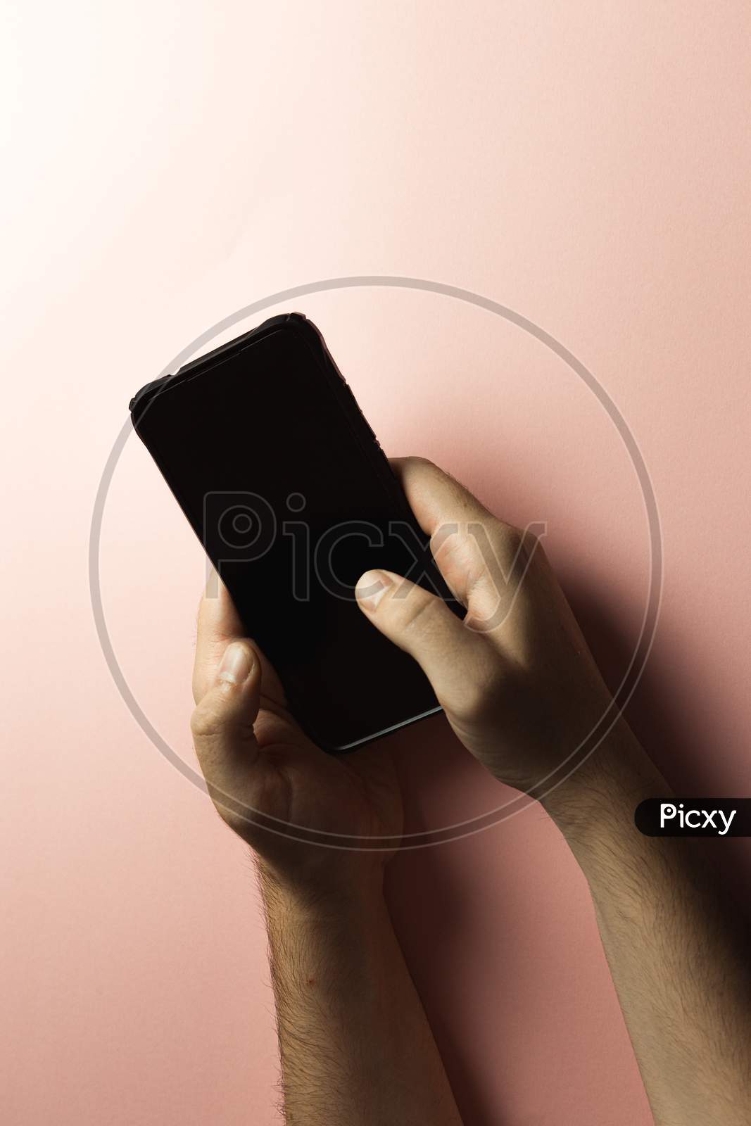 Top View Of Two Young Hands Using A Mobile Phone With Copy Space And A Black Screen Over A Pink Pastel Background
