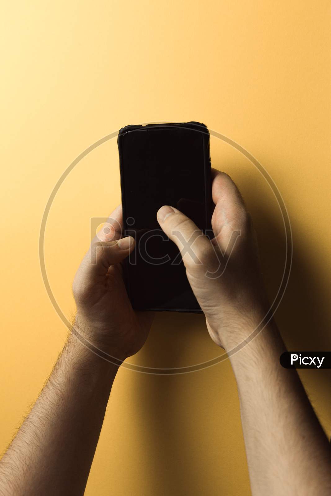 Top View Of Two Young Hands Using A Mobile Phone With Copy Space And A Black Screen Over A Pink Yellow Background
