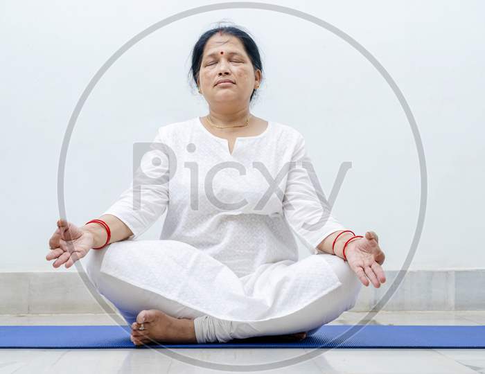 Middle Aged or an Old Indian Woman Performing Yoga Early Morning, in her house in white dress. Stay Home Stay Safe and Fit