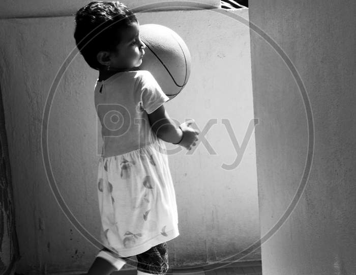 Vertical Shot Of Indian Girl Child Holding A Huge Ball In The Morning Sunlight