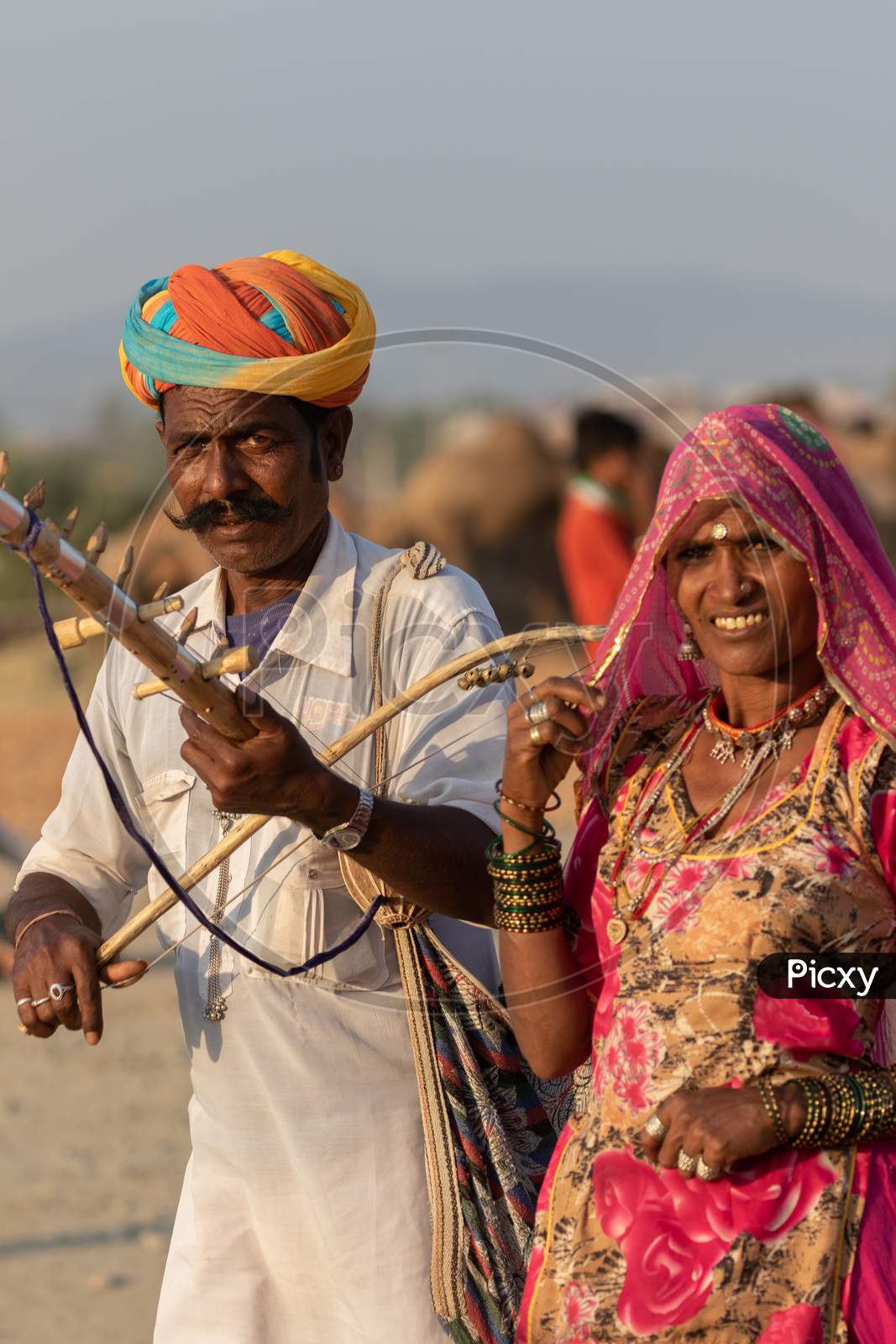 A man along with a women dressed in traditional rajasthani clothes playing musical instrument violin at Pushkar festival at Pushka