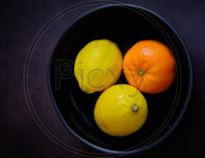 Lemon And Orange On Black Bowl In Dark Background