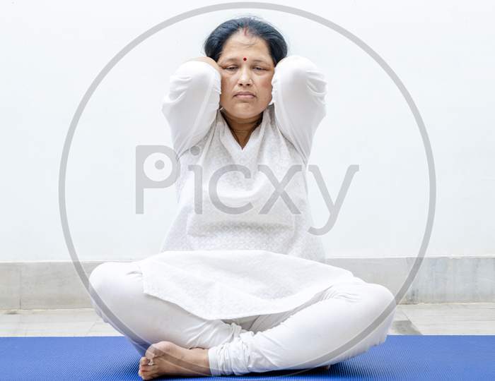Middle Aged or an Old Indian Woman Performing Yoga Early Morning, in her house in white dress. Stay Home Stay Safe and Fit