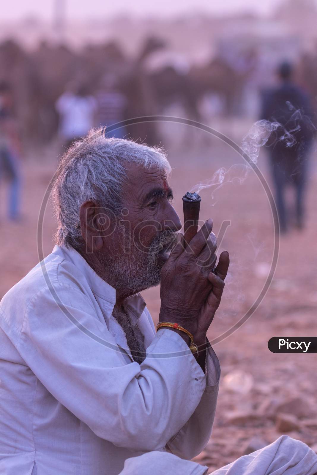 A rural Indian man siting an smoking tobacco inside a pipe at Pushkar, Rajasthan