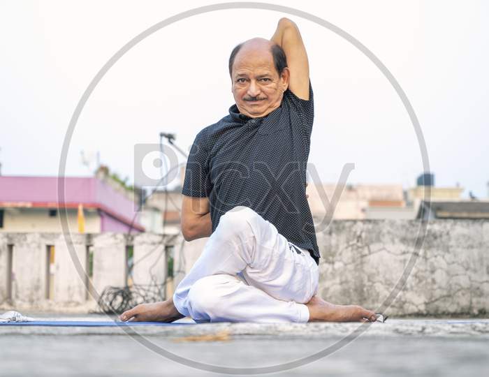 Senior Citizen or an Old Indian Man Performing Yoga Early Morning, in his Terrace in white Tshirt and Pants. Stay Home Stay Safe and Fit