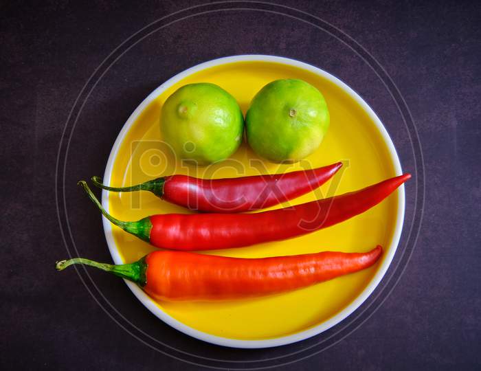 Red Chilli Pepper And Lemon On Yellow Plate In Dark Background