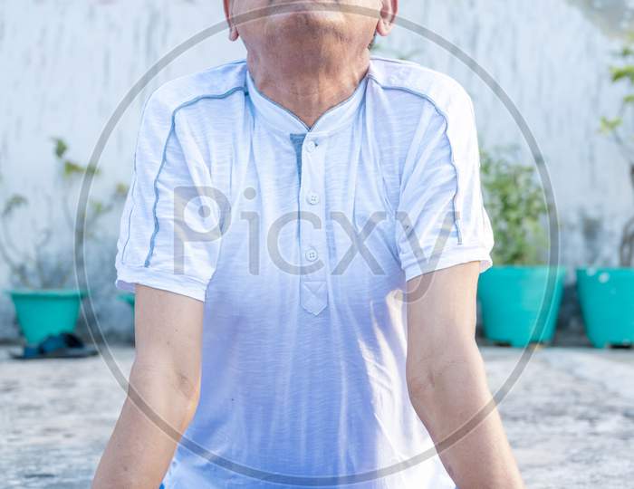 Senior Citizen or an Old Indian Man Performing Yoga Early Morning, in his Terrace in white Tshirt and Pants. Stay Home Stay Safe and Fit