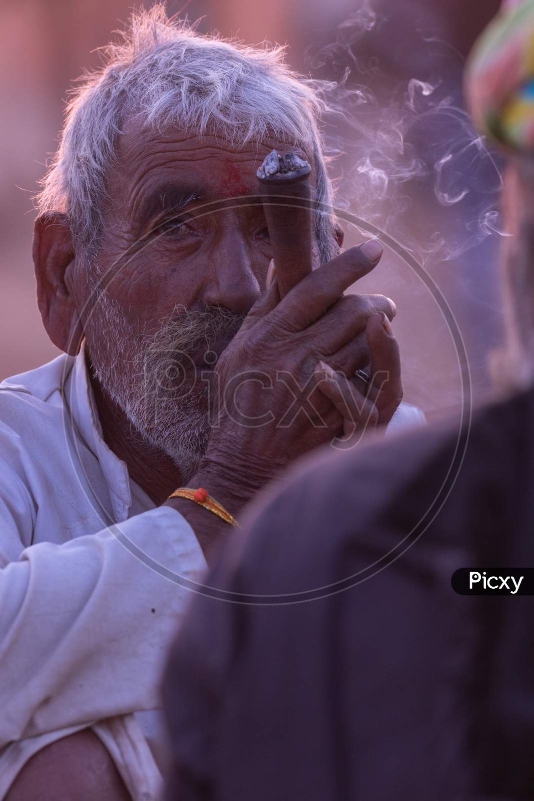 A rural Indian man siting an smoking tobacco inside a pipe at Pushkar, Rajasthan