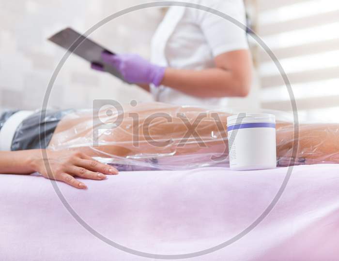 The Process Of Anti-Cellulite Vacuum Therapy With A Bag Is In Progress, And Next To The Patient'S Leg Is A Box Of Cream Used In The Process, And The Doctor Is Behind And Writes The Parameters.