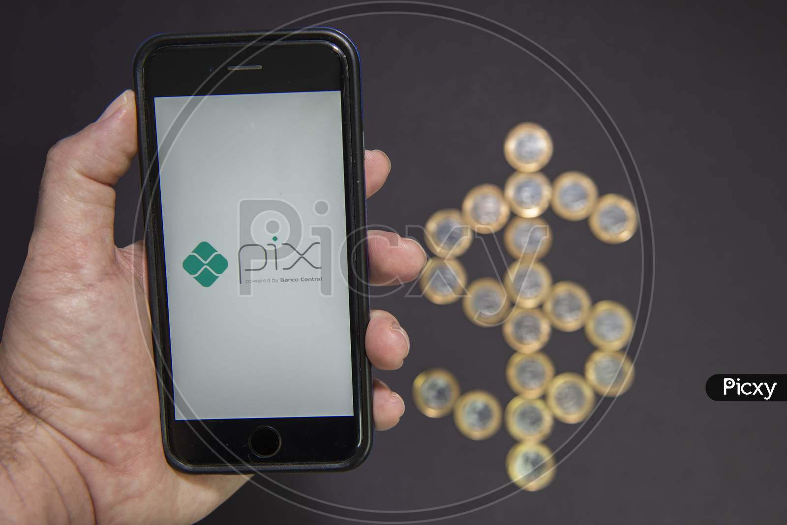 Florianopolis, Brazil. 07/10/2020: Man Hand Holding Smartphone With Pix Logo With Dollar Sign Made By 1 Real Coins On Background. Selective Focus. New Instant Payment System. Copy Space.