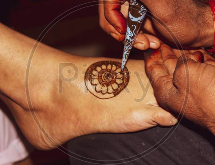 A view of a person hand applying Indian traditional Tattoo(Mehandi) on the feet for the festival