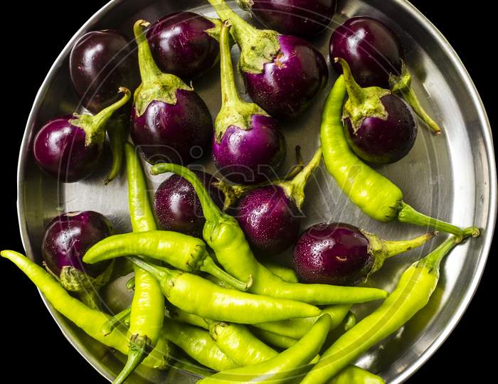 steel dish full of brinjal and green chillies, black background