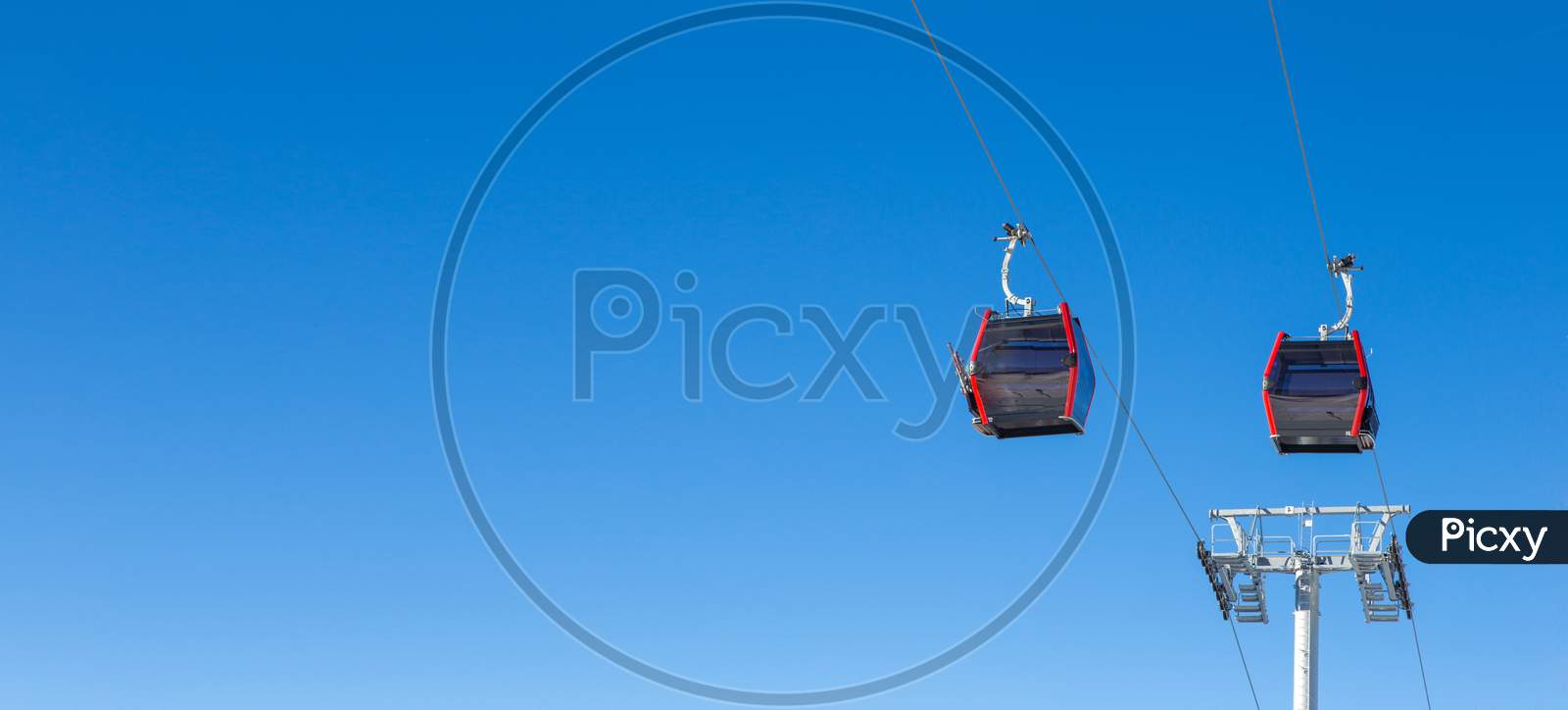 A Brand New Cable Car Is In Use. View Of Two Gondolas And Behind Them Is Clear Blue Sky. It'S A Beautiful Sunny Day On The Mountain.