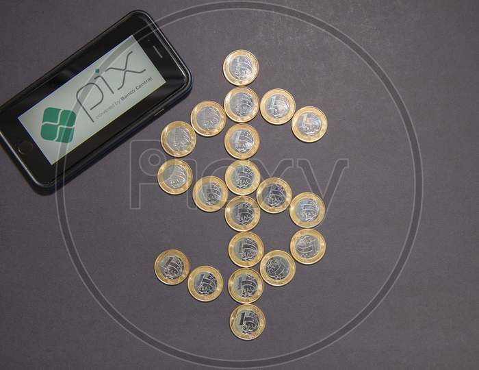 Florianopolis, Brazil. 10/07/2020: Pix Logo On The Smartphone Screen Next To Dollar Sign Made By 1 Real Coins On Black Background. New Instant Payment System. Copy Space.