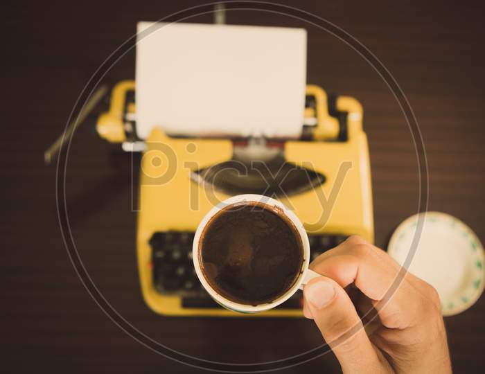 The Writer Is In Front Of An Old Yellow Typewriter And He'S Drinking Coffee And Waiting To Get Inspiration.