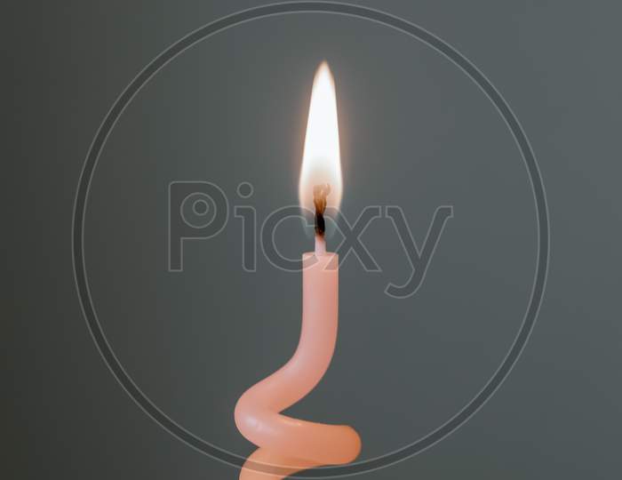Burning pink candle against gray background