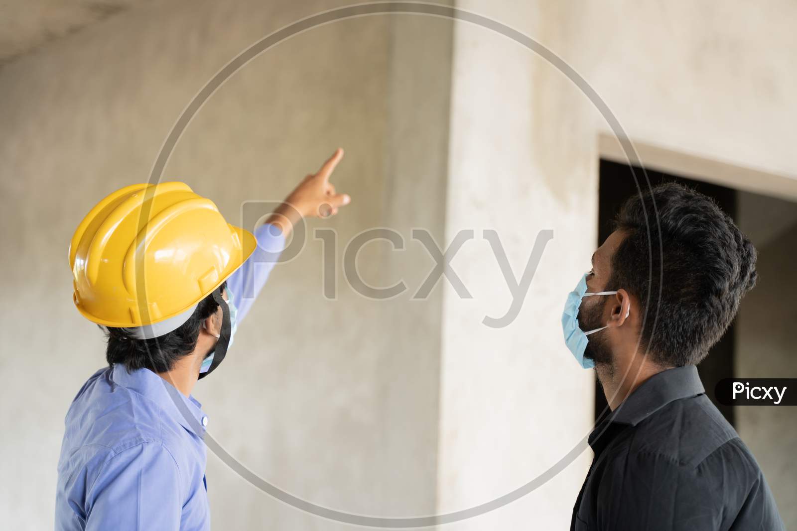 Two Construction Worker In Medical Mask Busy In Work While Maintaining Social Distancing - Concept Of Covid-19 Or Coronavirus Safety Measures At Work Place.