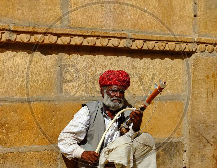 A man wearing turban is siting on ground and playing vilolin at Jaiselmer Rajasthan