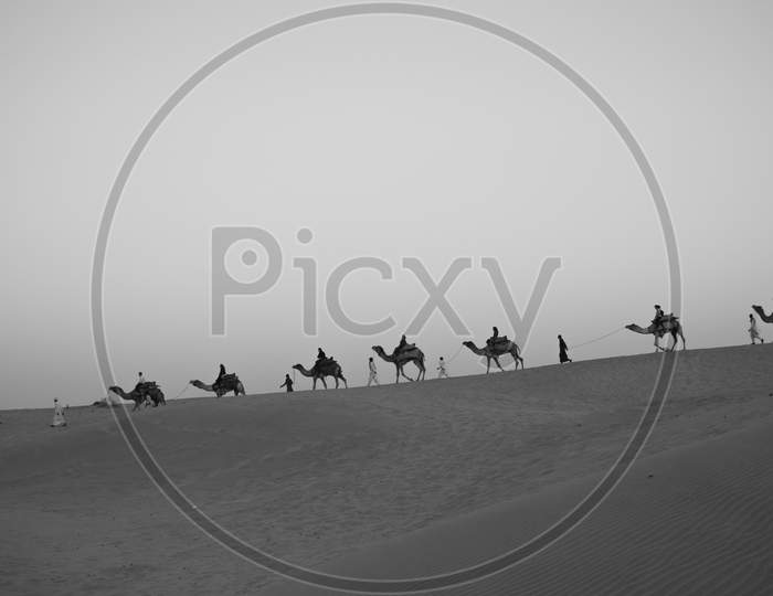 Silhouette of a line of camels walking on Sam sand dunes with people
