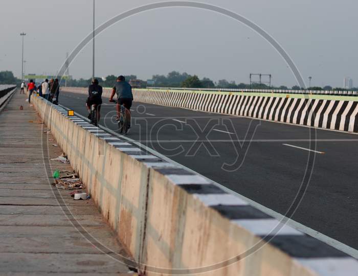 A Crowd Of People Gathered On The Road Built On The River Bridge And Some Players Cycled.