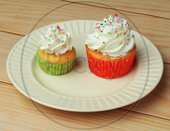 Different Types Of Vanilla Cupcakes With White Butter Cream Frosting And Sprinkles On White Plate For Birthday Celebration