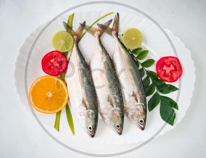 Fresh Indian Mackerel Fish Decorated With Herbs And Vegetables On A White Plate.