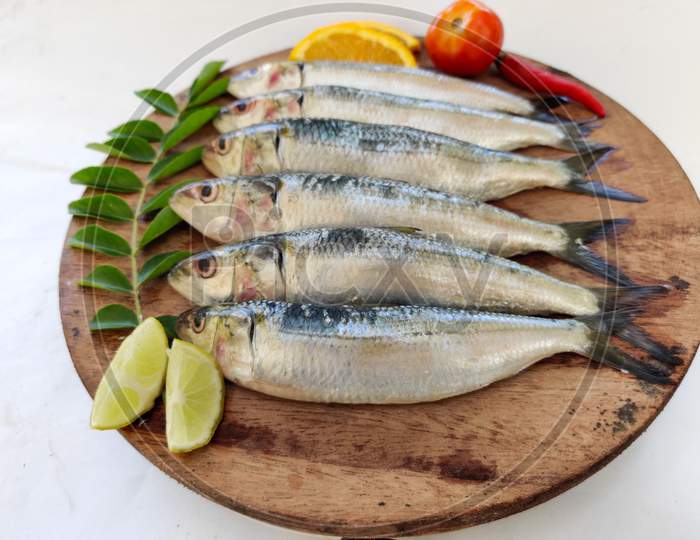Close Up View Of Fresh Indian Oil Sardine On A Wooden Pad,Decorated With Herbs And Vegetables.White Background.