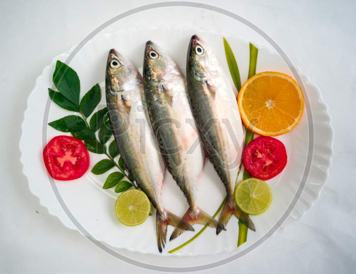Fresh Indian Mackerel Fish Decorated With Herbs And Vegetables On A White Plate.