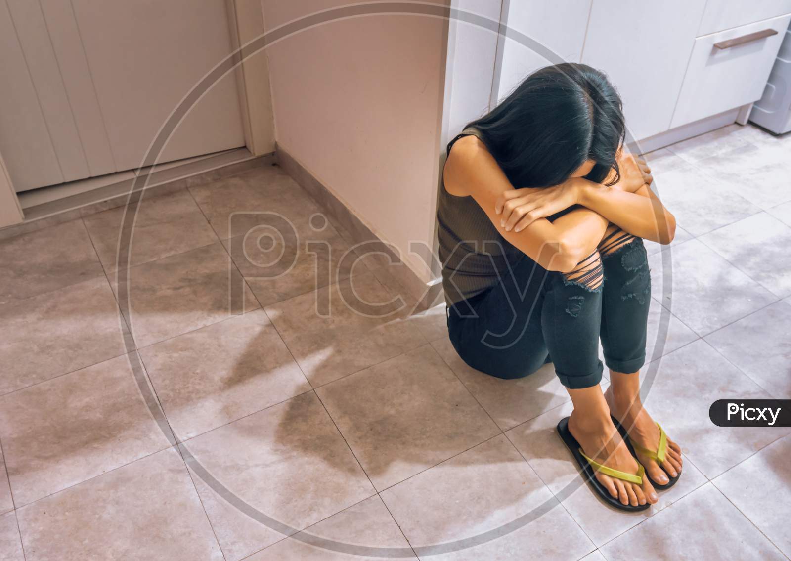 Young Black-Haired Caucasian Woman  Sits On The Floor Covering Her Face With Huging Her Knees. Concept Of Anxiety And Depression.