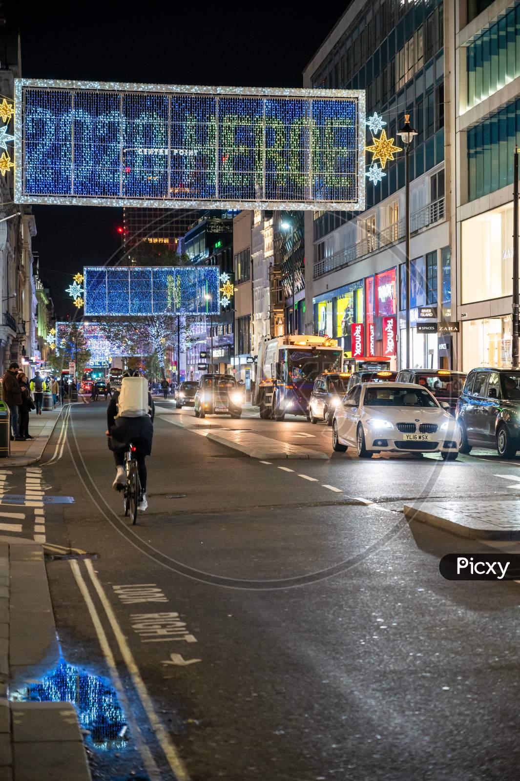 A Cyclist Rides Along Oxford Street Beneath The Christmas Decorations At Night