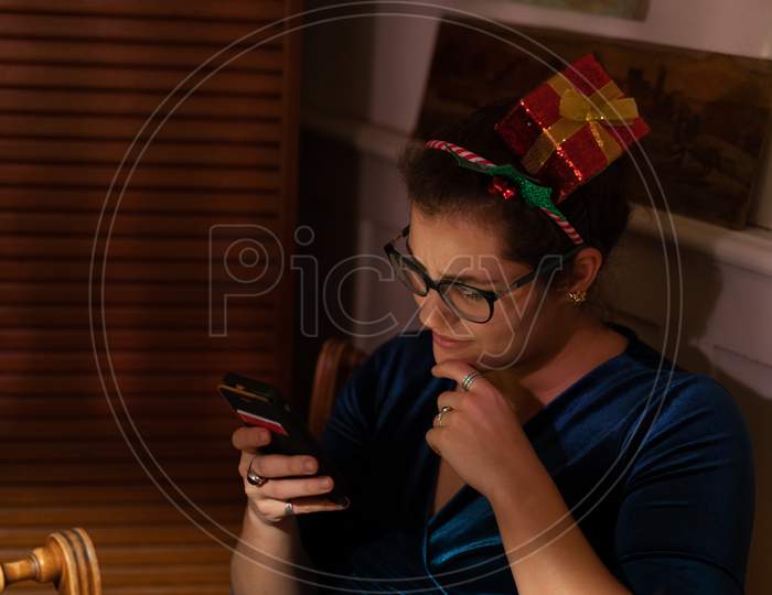 Young Woman Is Lost In Thoughts Looking Into Her Mobile Phone At Christmas.