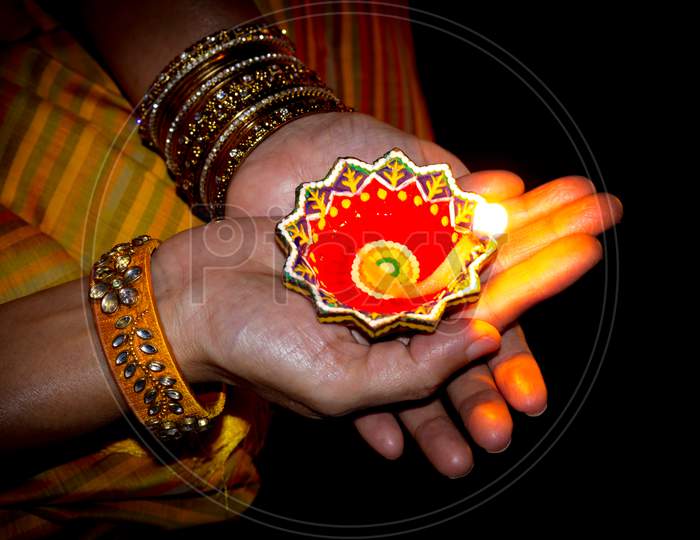 A divine view of a Lady's hands holding a traditional Diya or Lamp emitting  soft golden light for the Deepavali festival which is Celebrated across the Indian States.