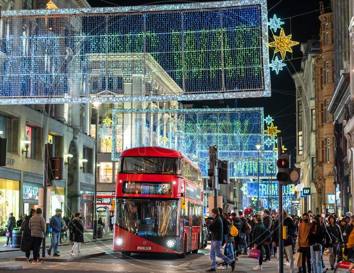 Shoppers And A London Red Double Decker Bus Beneath The Oxford Street Christmas Decorations At Night