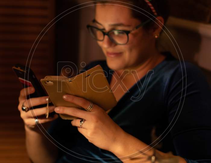 Smiling Young Woman Looking Into Her Cellphone At Christmas. Focus On Foreground