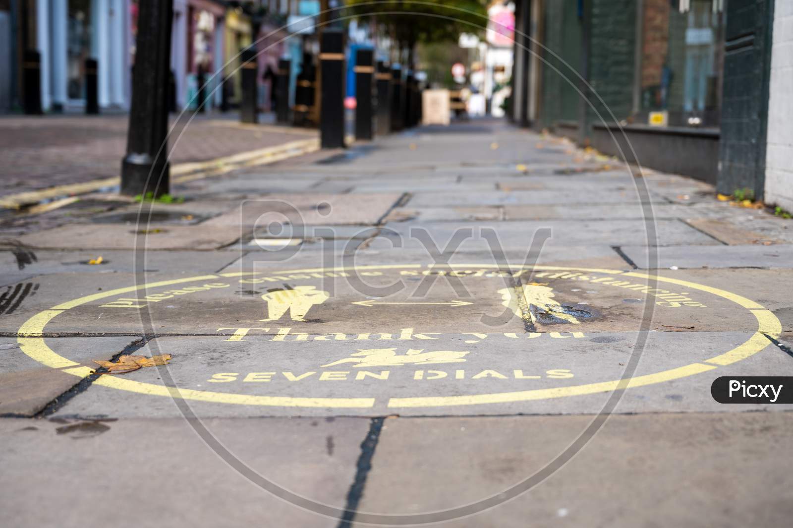 Yellow Covid 19 Social Distancing Sign Painted On The Ground In Covent Garden With A Street Out Of Focus In The Background