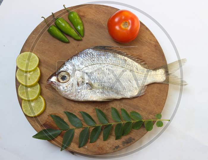 Gerres Fish (Gerres Filamentosus) / Whipfin Silver Biddy Fish , Decorated With Curry Leaves And Tomato On A Wooden Pad,White Background.