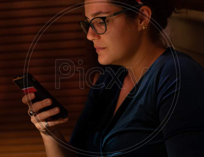 Young Woman Looking Thoughtful Into Her Cellphone At Christmas.