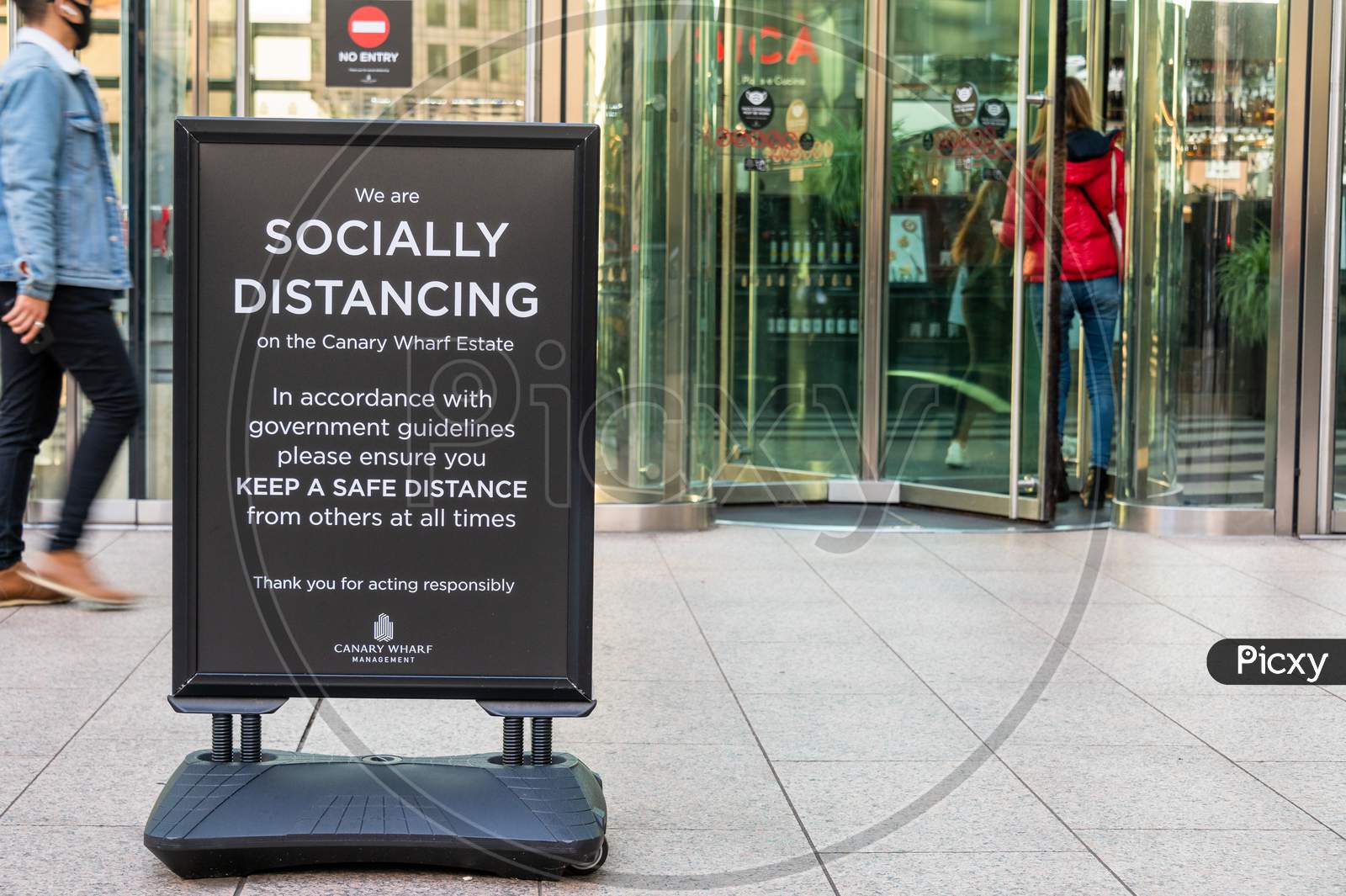 Covid 19 Social Distancing Sign Outside A Building In Canary Wharf With Revolving Doors In The Background