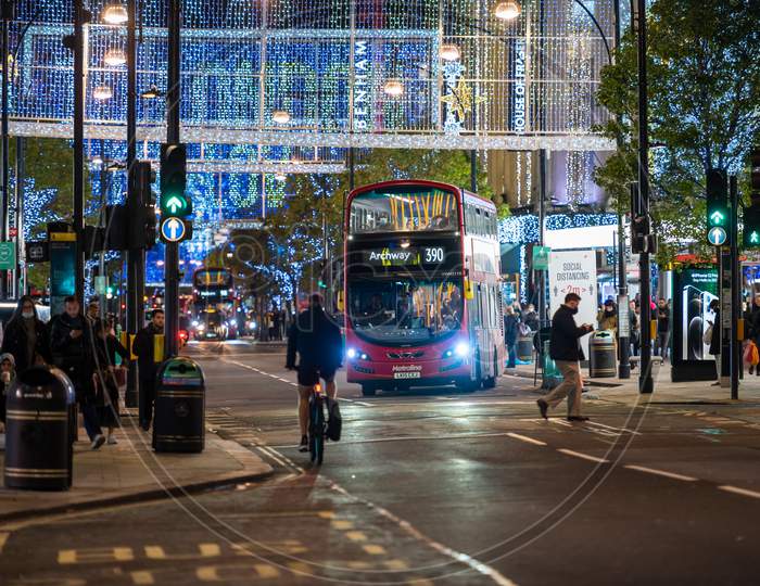 Red London Double Decker Bus Pulling Away From Bus Stop On Oxford Street Illuminated By Christmas Lights