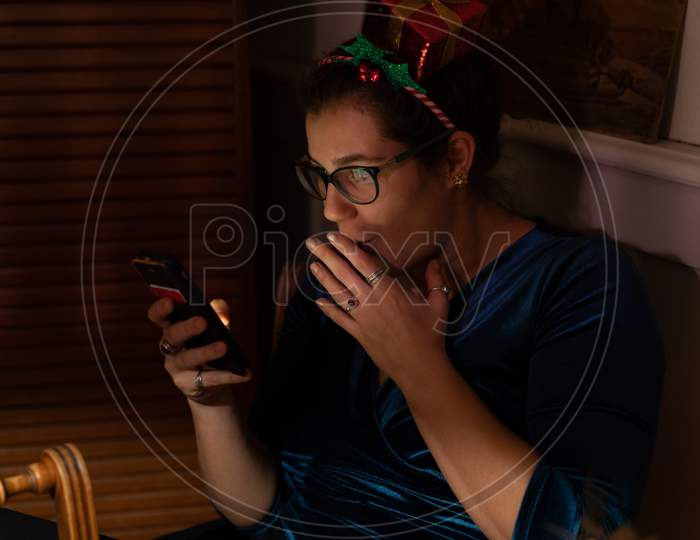 Amazed Young Woman Looking Into Her Phone At Christmas.