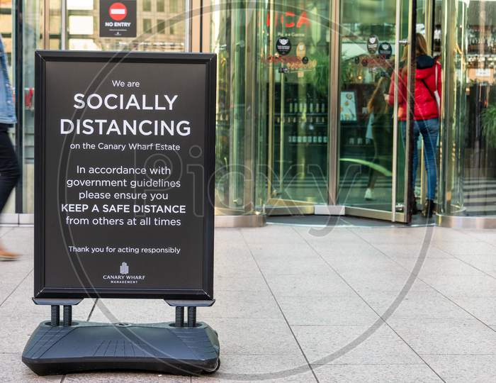 Covid 19 Social Distancing Sign Outside A Building In Canary Wharf With Revolving Doors In The Background