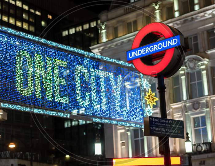 London Underground Sign At Oxford Circus With Illuminated Oxford Street Christmas Decorations Out Of Focus In The Background