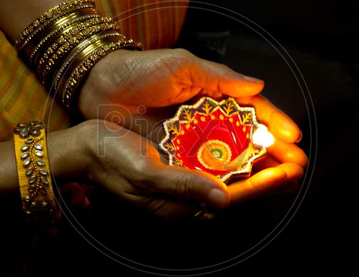 A Dramatic view of an Earthen lamp emitting  soft golden light placed in a Lady's palms for the  Diwali festival which is Celebrated across the Indian States.