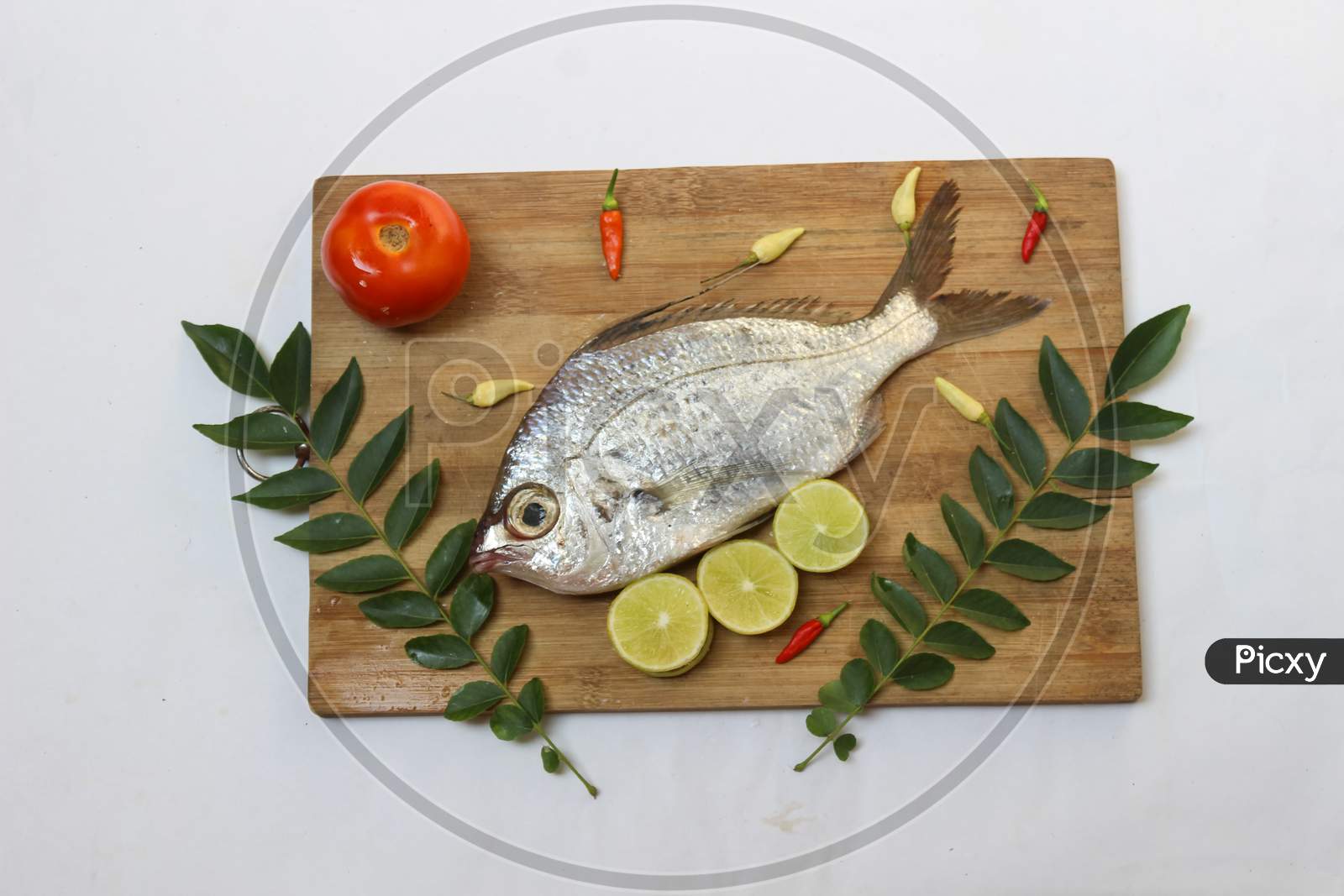 Gerres Fish (Gerres Filamentosus) / Whipfin Silver Biddy Fish , Decorated With Curry Leaves And Tomato On A Wooden Pad,White Background.