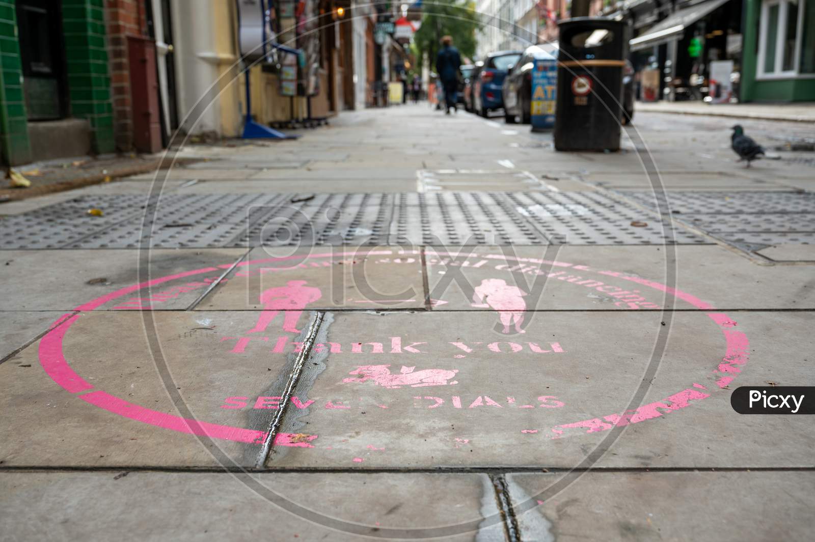 Pink Covid 19 Social Distancing Sign Painted On The Ground In Covent Garden With A Street Out Of Focus In The Background