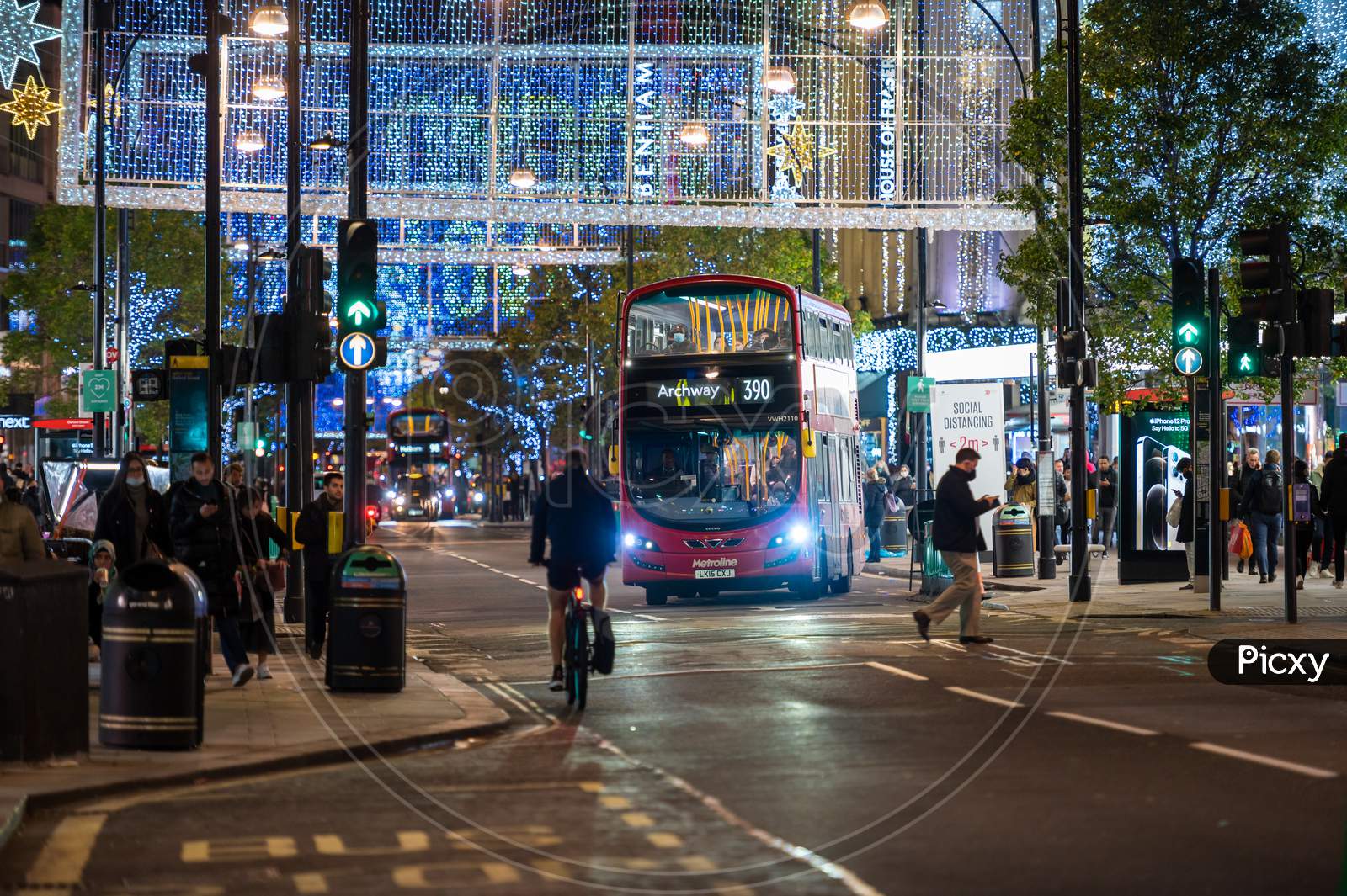 Red London Double Decker Bus Pulling Away From Bus Stop On Oxford Street Illuminated By Christmas Lights