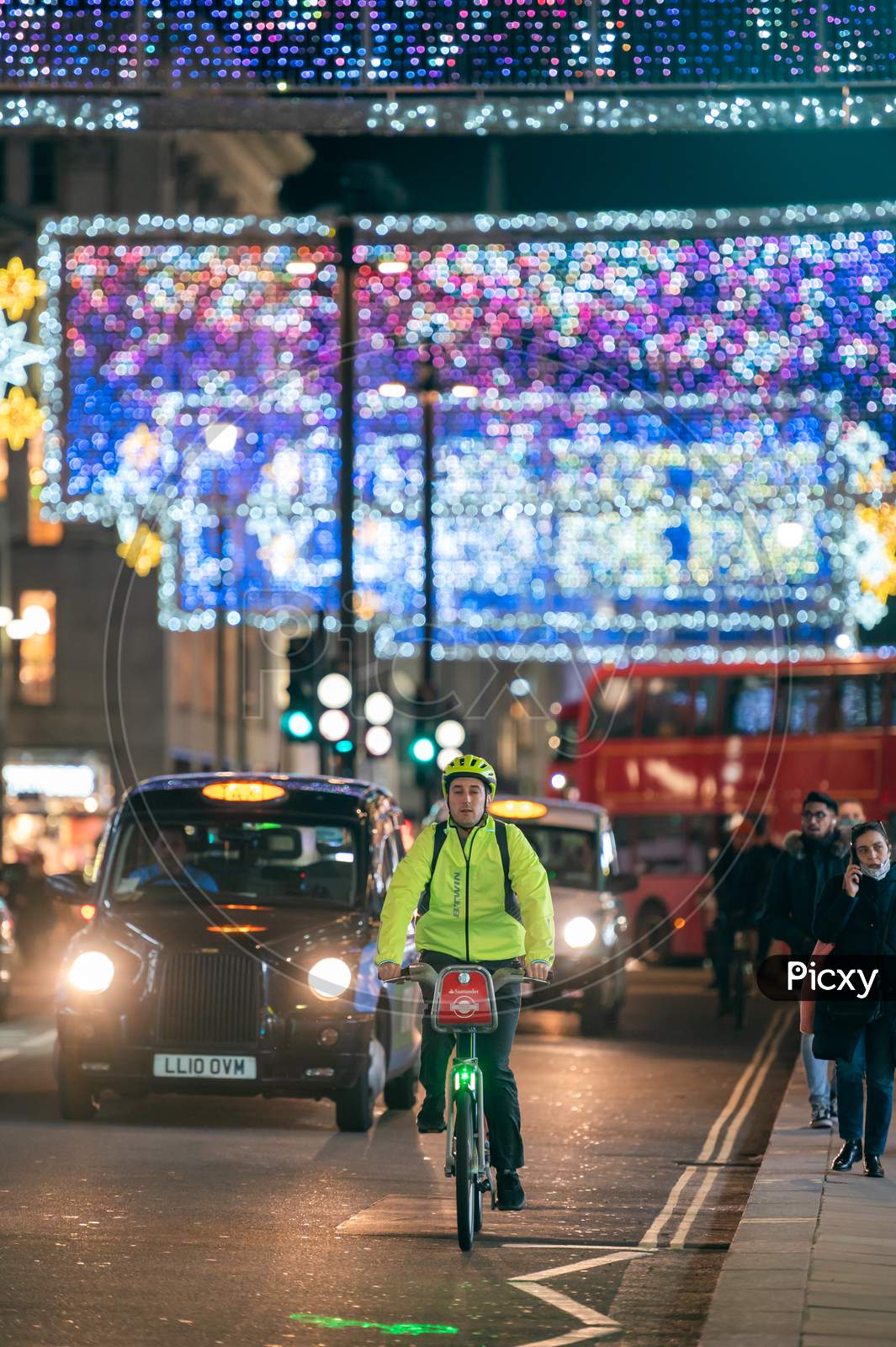 A Cyclist And A Black London Taxi Cab With Oxford Street Illuminated Christmas Decorations In The Background