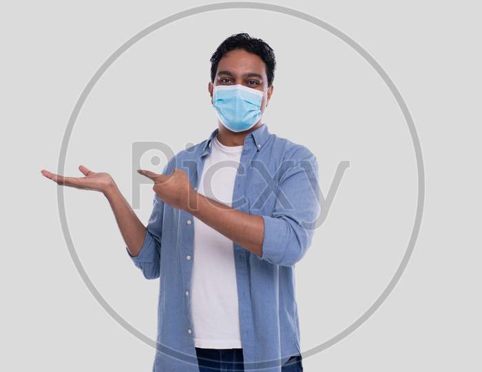 Man Showing Hand To Side And Pointing At It Wearing Medical Mask Isolated. Indian Man Wearing Medical Mask