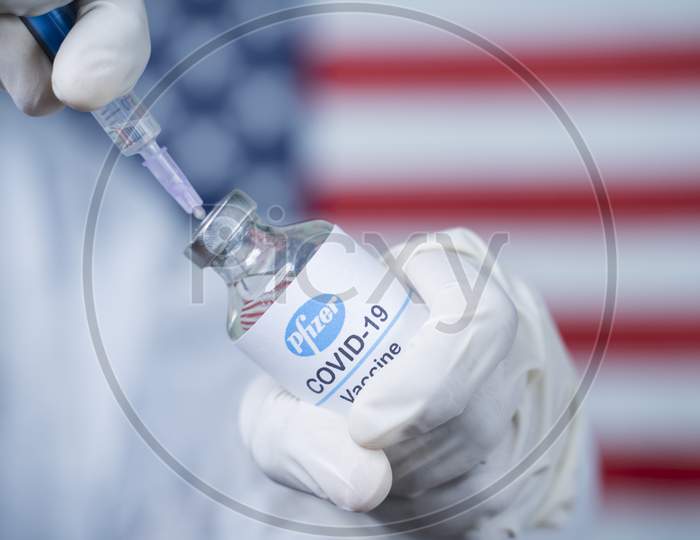 Maski, India - Nov 12,2020 : Doctor Holding Pfizer Biontech Vaccine And Syringe To Protect Against Coronavirus Covid-19 Disease With Us Flag As Background.